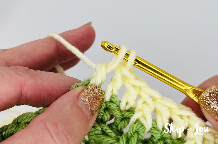 Yellow yarn is being pulled up on a gold hook to create a waffle stitch.