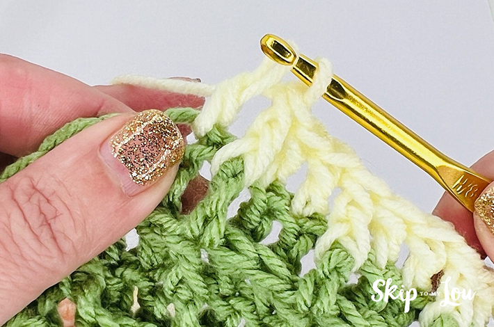 Yellow yarn is being pulled up on a gold hook to create a waffle stitch.