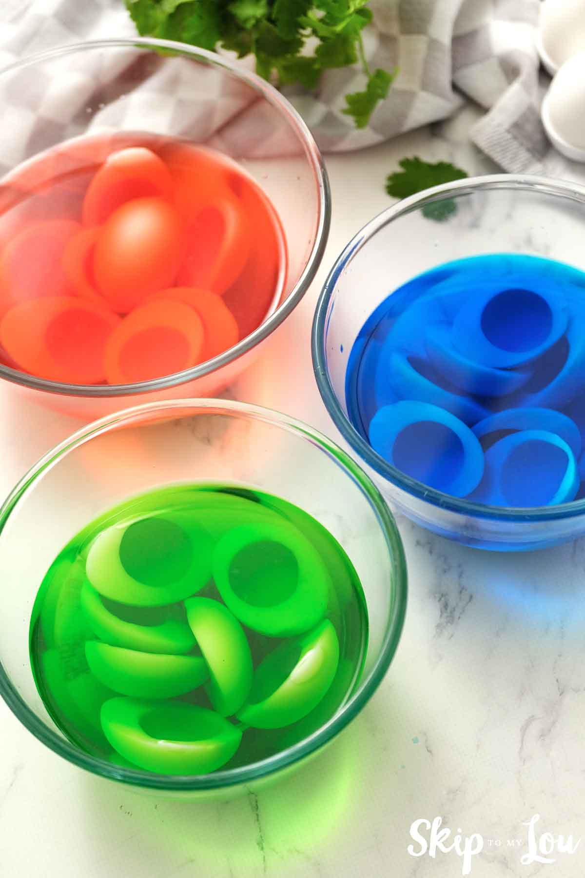 bowls filled with red green and blue food coloring with hard boiled eggs in the dye