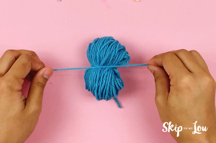 Tightening a piece of string around the wool to tie the pom pom tight.