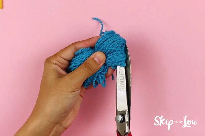 Cutting the tight ends of the pom pom with scissors.