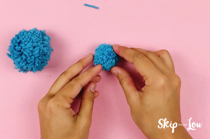 The perfect pom pom. A blue pom pom held by two hands over a pink background.