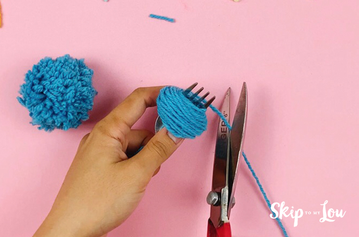 A scissors cutting the wool from a pom pom of the desired size.