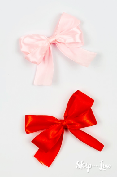 Finished result of DIY bows made from ribbon, one is red and the other one is pink, on top of a white backgrond.