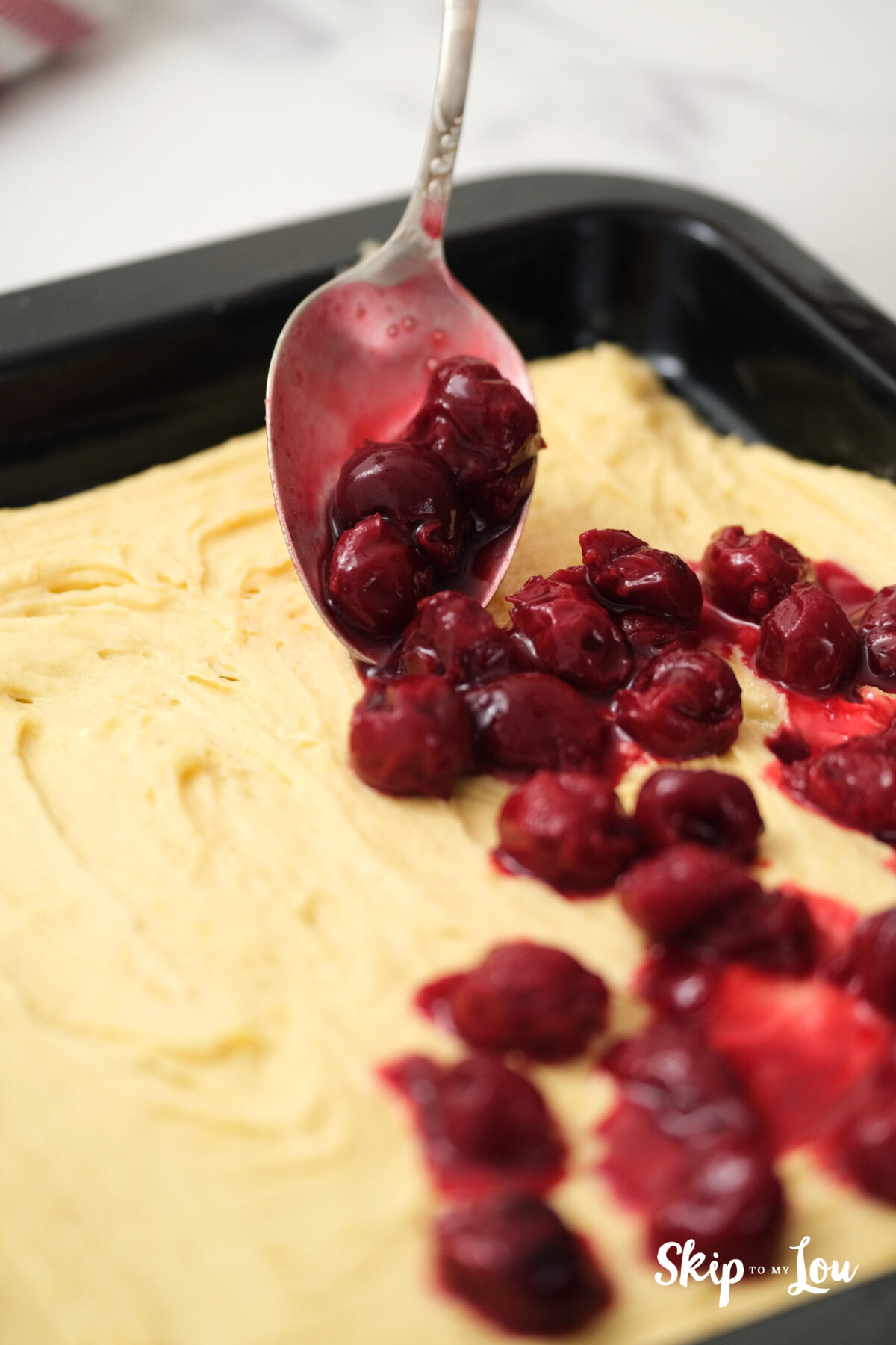 Batter spread on a tray and topped with cherries and their juice.