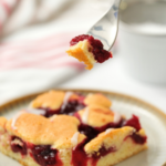Image shows a cherry coffee cake and a fork holding a part of it, on a nice bright background