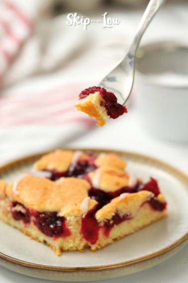 Image shows a cherry coffee cake and a fork holding a part of it, on a nice bright background
