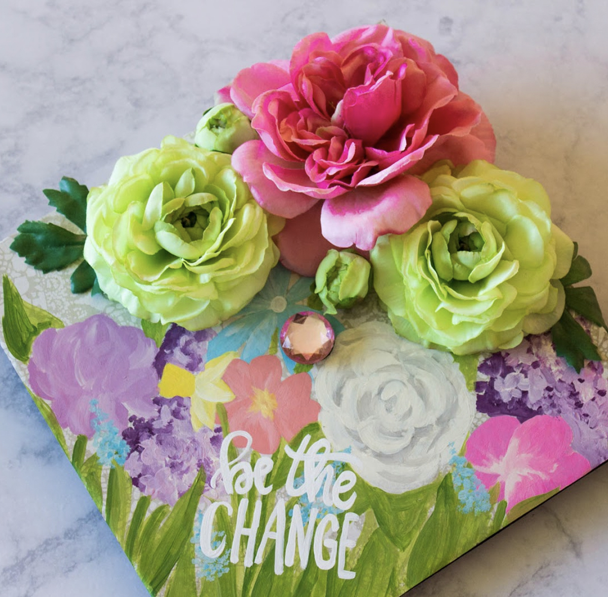 Graduation cap decorate with fake green and pink flowers and quote that says "be the change"