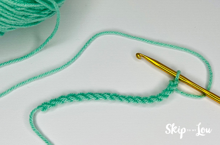 Green yarn and a crochet needle forming the foundation  row for the granny stitch.