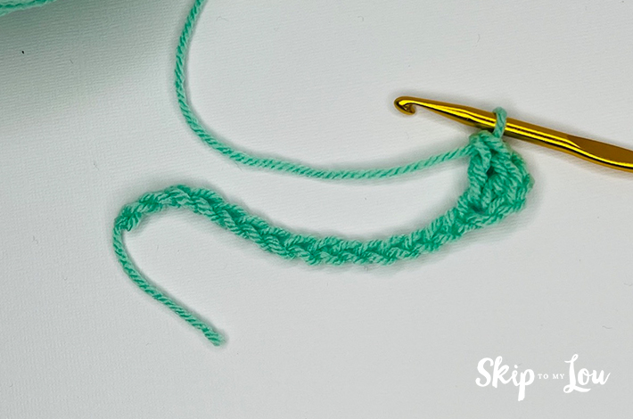 Green yarn and a crochet needle forming the second  row for the granny stitch.