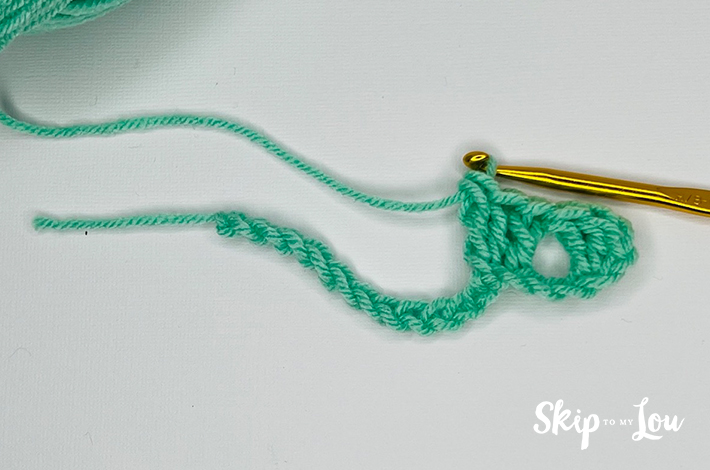 Green yarn and a crochet needle forming the third row for the granny stitch.