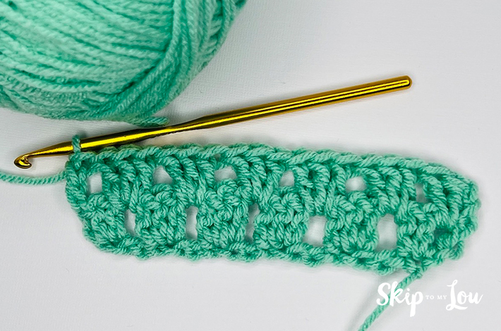 Green yarn and a crochet needle forming the fourth row for the granny stitch.