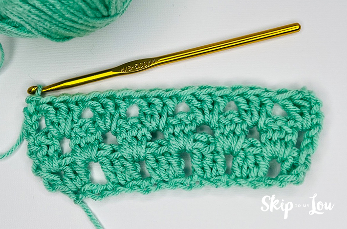 Green yarn and a crochet needle forming the fifth row for the granny stitch.