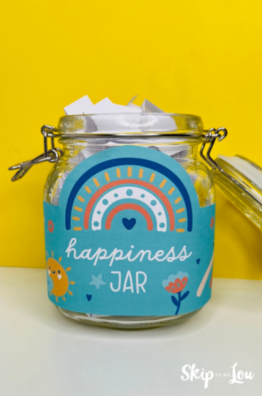 Picture of a happiness jar - a mason jar filled with notes, and is decorated with a blue label that says "happiness jar". Idea from Skip to my Lou