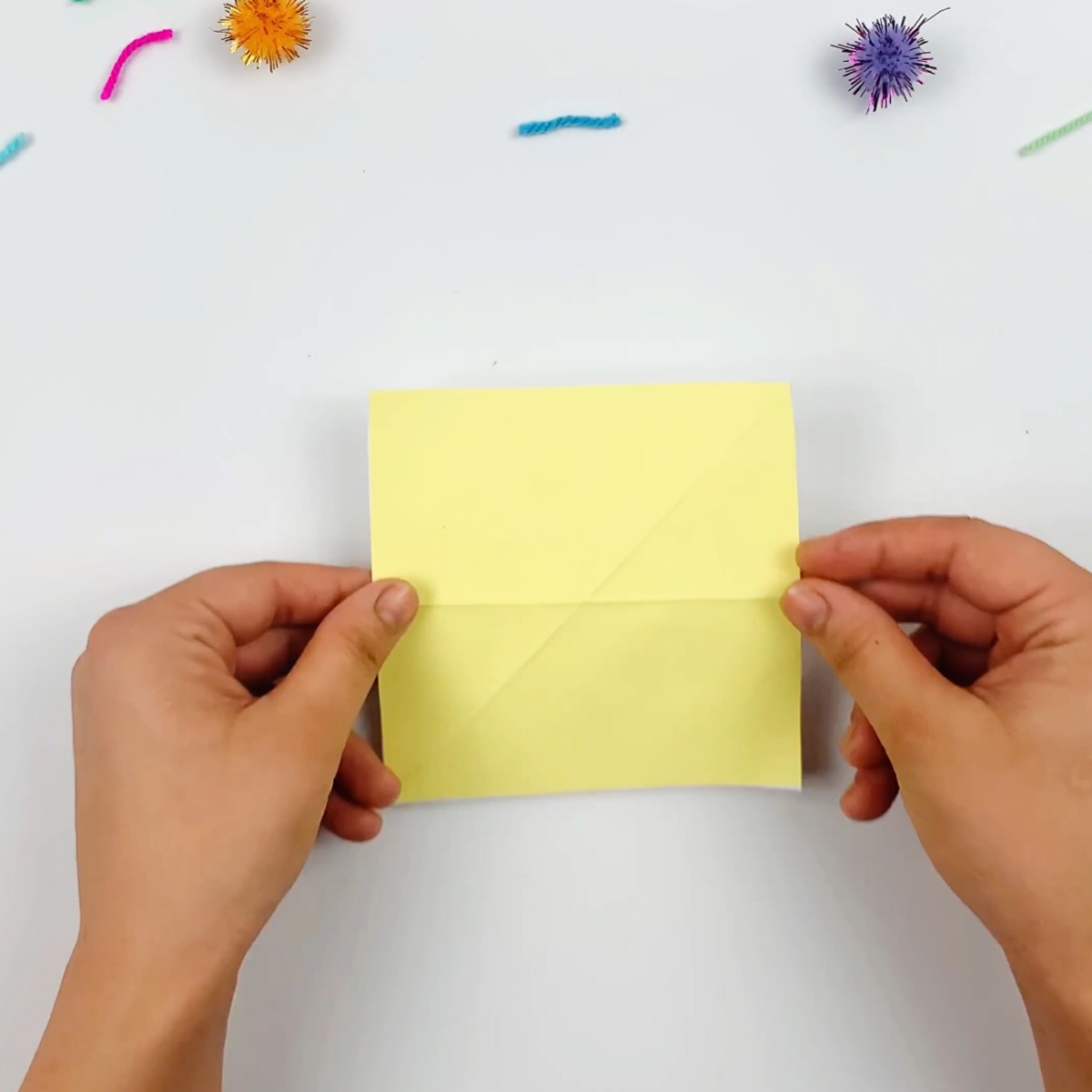 A yellow piece of paper ready to be folded for the origami cat's head.