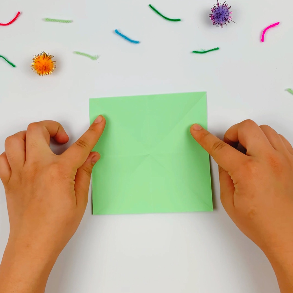 A square piece of green paper about to get folded to start the origami fish.