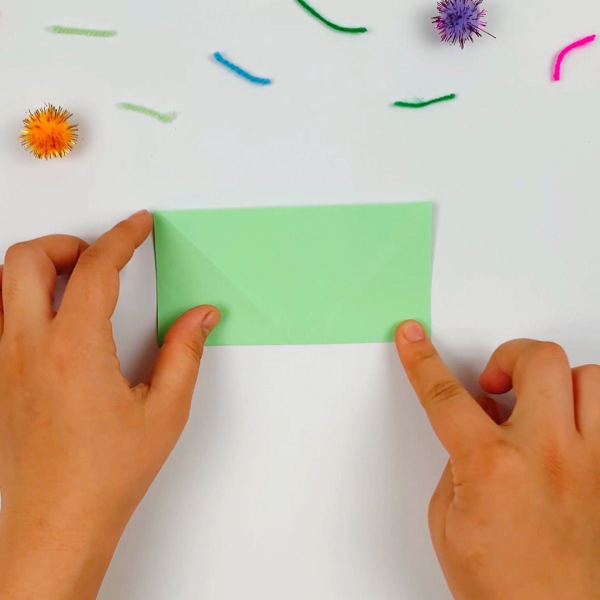 The square green paper is folded in half.