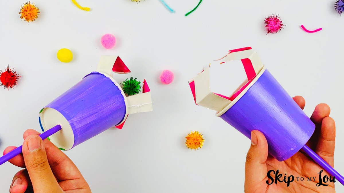 Two paper cup mechanical claws picking up pom poms.