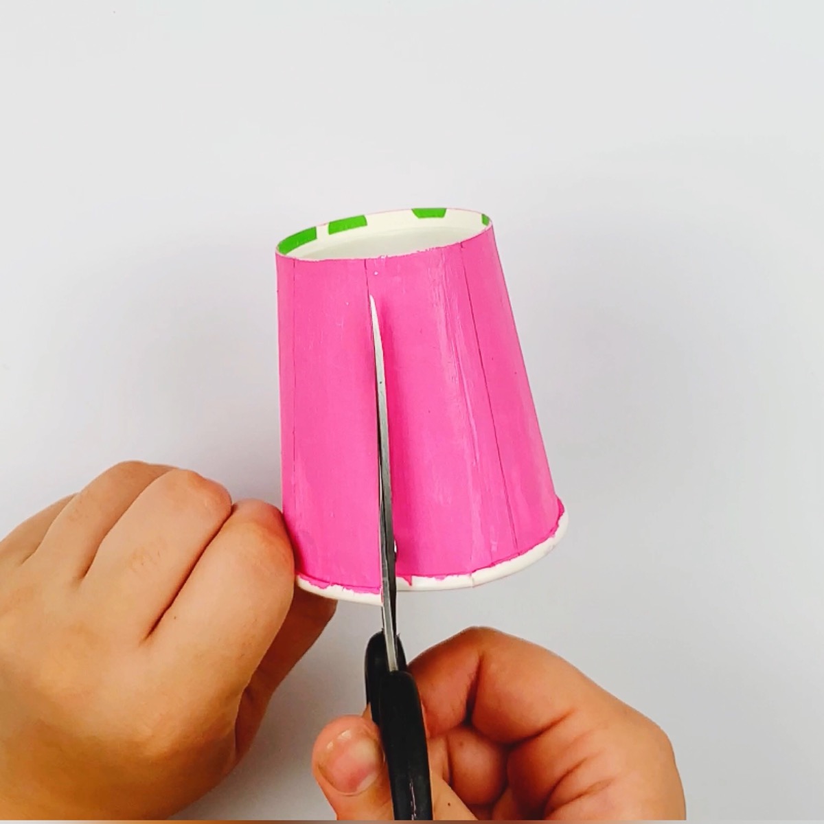A paper cup being cut with a scissors, as the first step in making a mechanical claw.