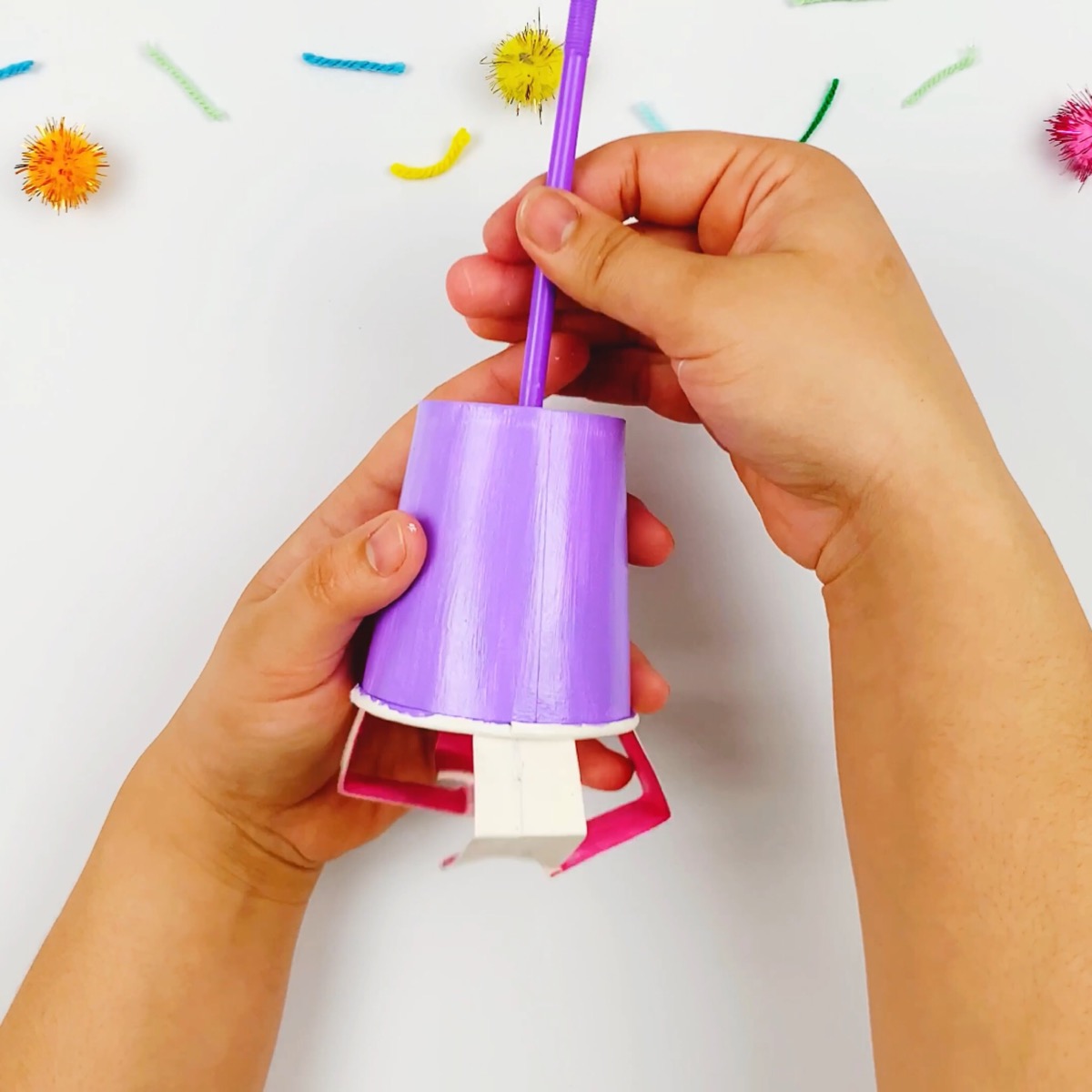 Placing the mechanical claw and the straw through the hole in the second paper cup.