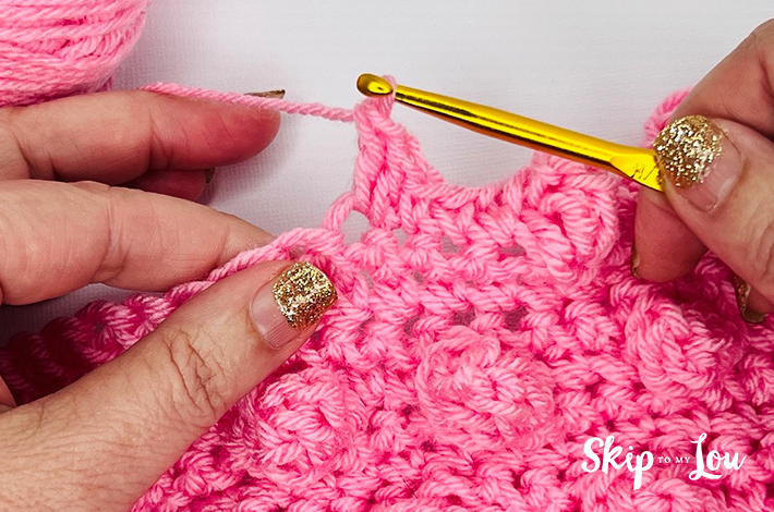 Two hands holding a crochet hook and working with pink yarn on the 8th step of the popcorn stitch.