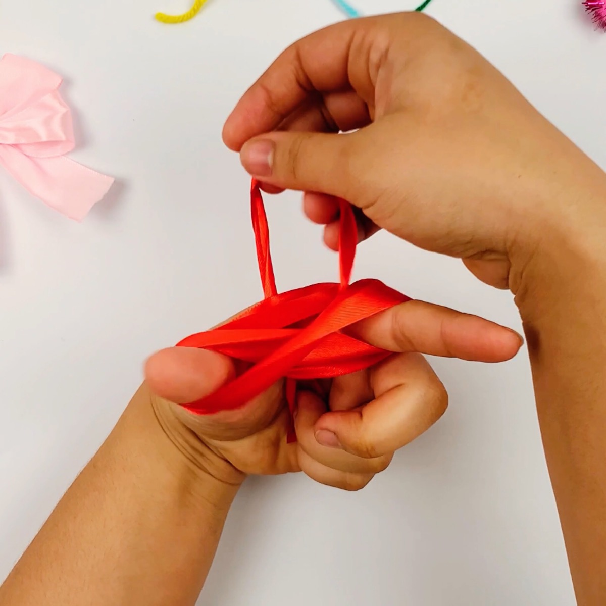 Step 7 of the ribbon bow making process showing how the ribbon is pulled all the way through leaving two bow shapes between the thumb and index finger.