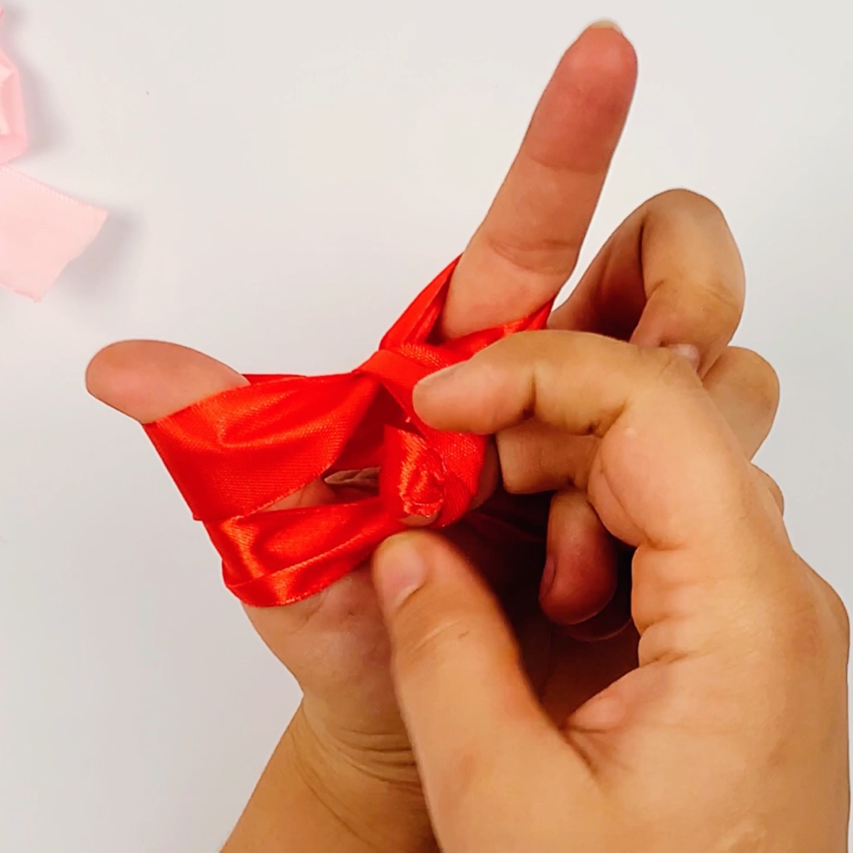 Step 9 (part 1) of the ribbon bow making process showing how the ribbon is secured in the center.