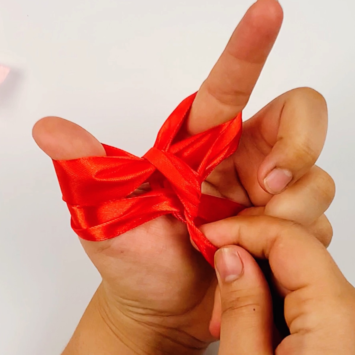 Step 9 (part 2) of the ribbon bow making process showing how the ribbon is wrapped around the index finger for a second time.