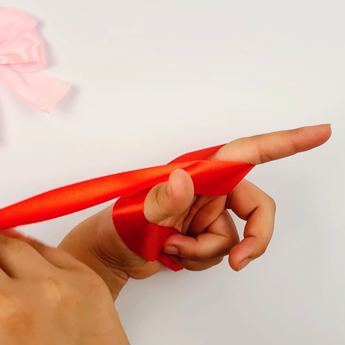 Step 2 of the ribbon bow making process showing how the ribbon is wrapped around the index finger.
