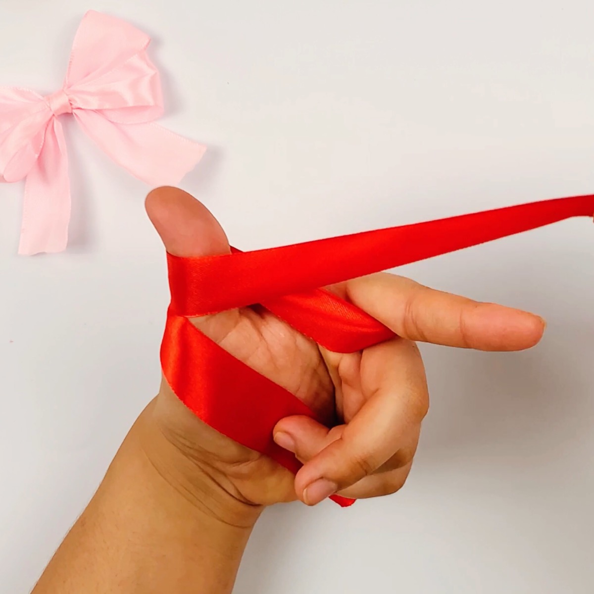 Step 3 of the ribbon bow making process showing how the ribbon is wrapped around the thumb for a second time.