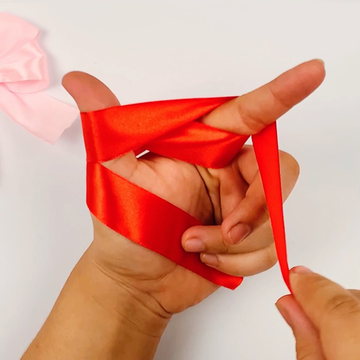 Step 4 of the ribbon bow making process showing how the ribbon is pulled down toward the palm.