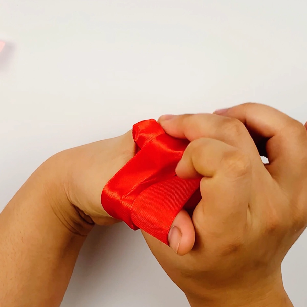 Step 6 of the ribbon bow making process showing how the ribbon is pulled out underneath towards the back of the hand.