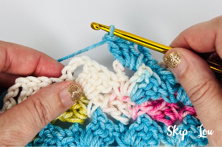 Hands holding a crochet needle crocheting the first part of the traditional tulip stitch.