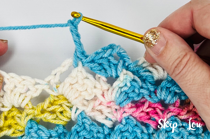 Hands holding a crochet needle crocheting the second part of the traditional tulip stitch.