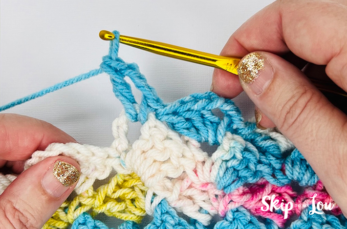 Hands holding a crochet needle crocheting the second part of the traditional tulip stitch and showing two completed lines.