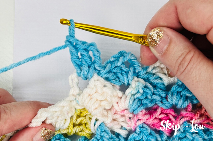 Hands holding a crochet needle crocheting the third part of the traditional tulip stitch.