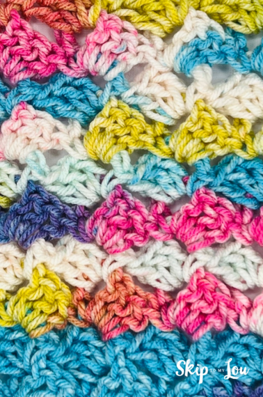 A tulip crochet stitch made up fo light blue, pink, orange, white, purple and yellow yarn from Skip to My Lou.