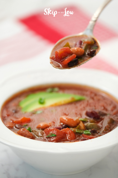 A steaming bowl of vegetarian chili using beans, carrot, avocado, and other vegetables, made from a Skip to My Lou recipe.