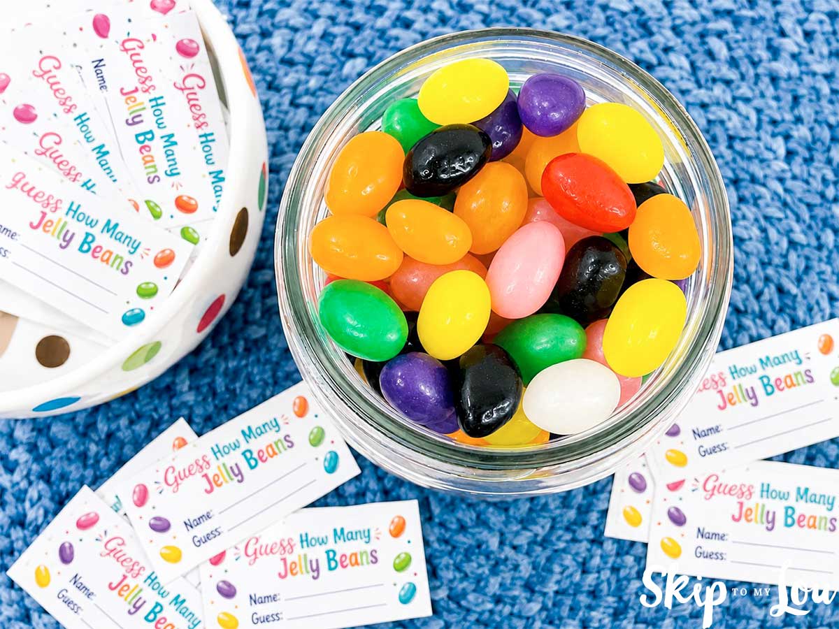 Top view of colorful jelly beans in a mason jar with printable guess cards around it