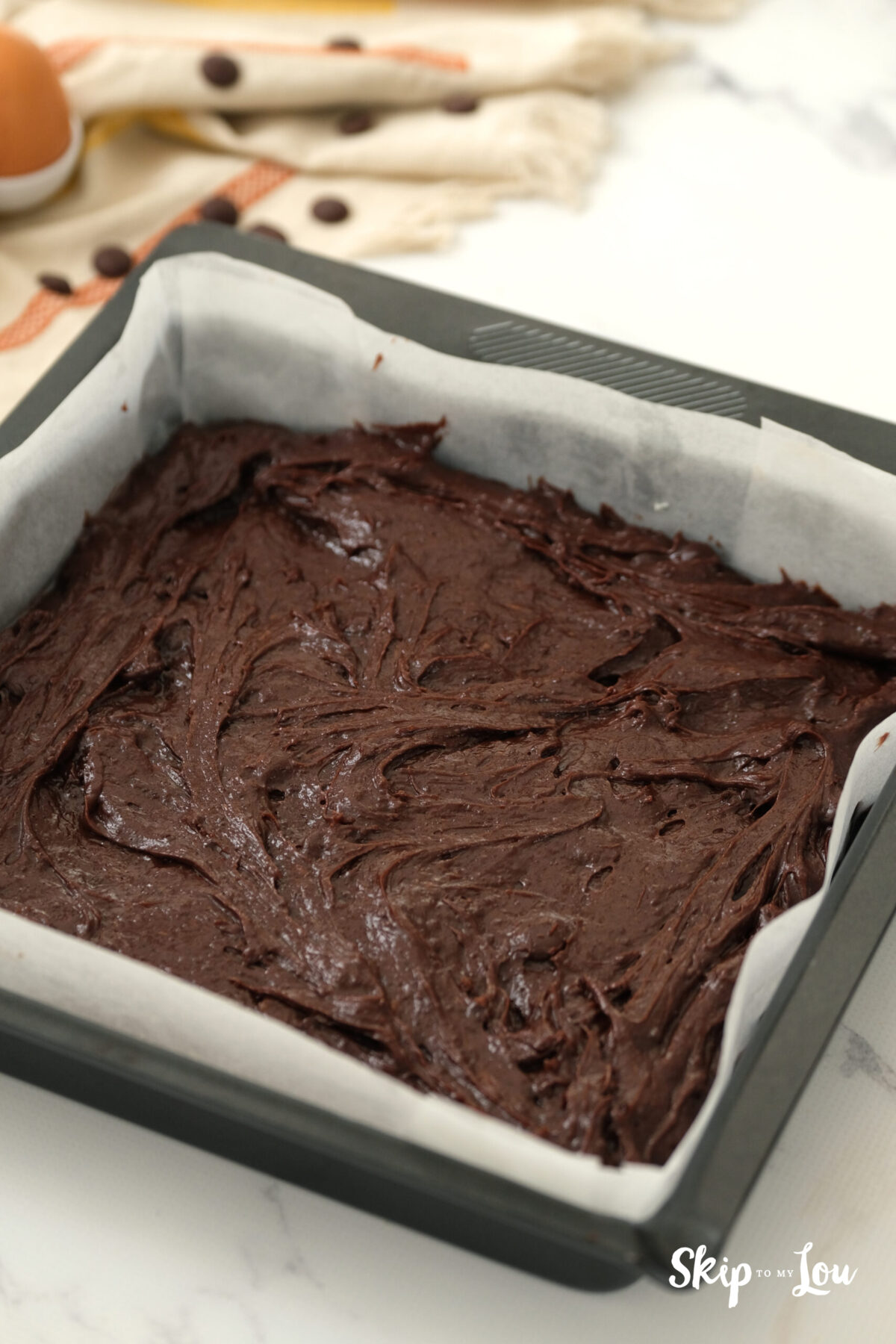 The brownie batter spread of parchment paper in a baking tray.