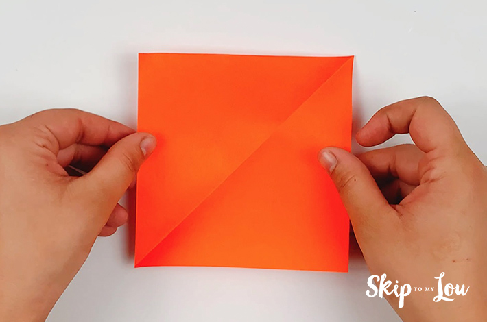 A square piece of orange paper about to get folded to start the origami leaf.
