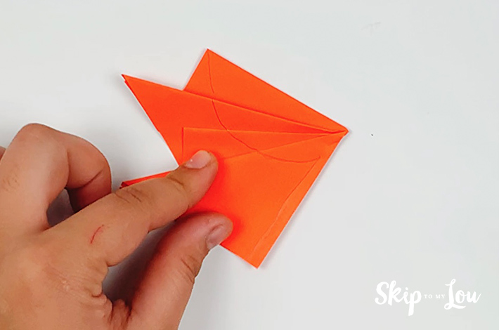 After all the folds, the paper is ready to be cut into a leaf shape. A line is drawn on the paper to guide the scissor work.