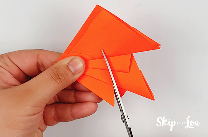 Using a pair of scissors, the folded paper is cut along the line.