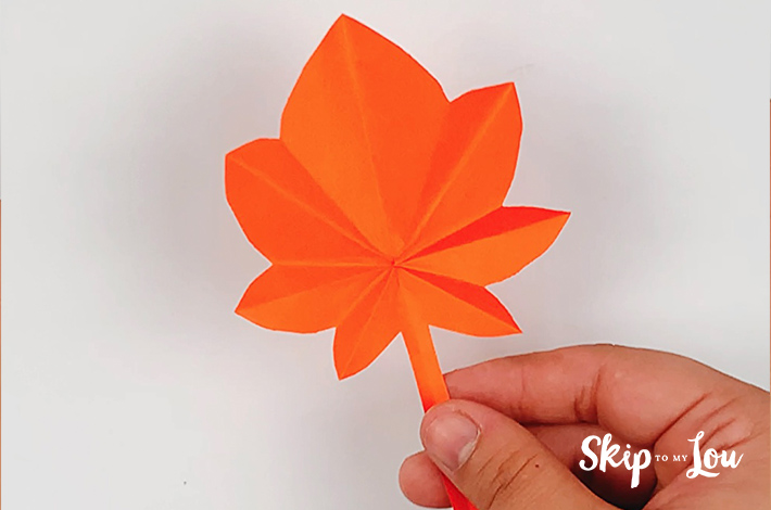 A hand holding a completed origami leaf.