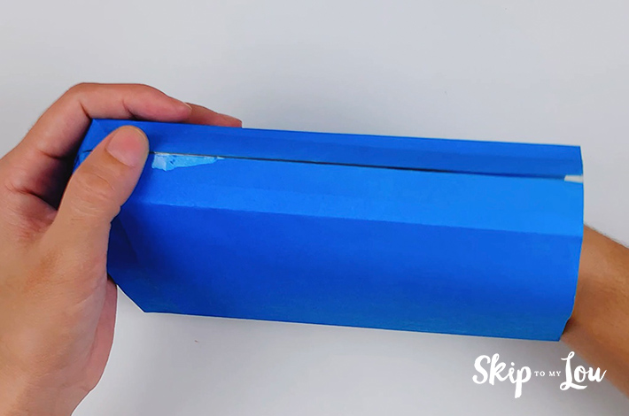 A hand is placed in the top opening to form a rectangular box shape for the origami shirt and tie. 