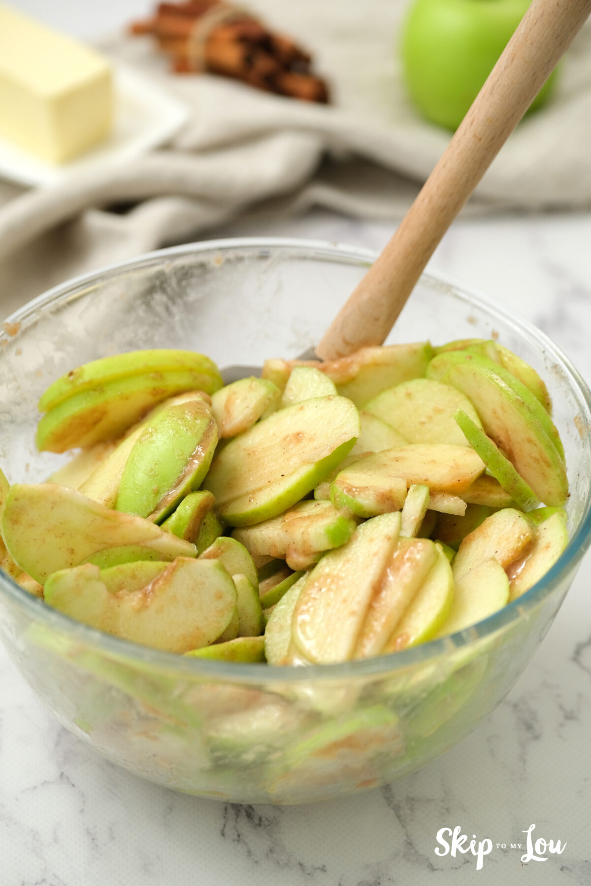 The dry ingredient being tossed through apple slices in a bowl.