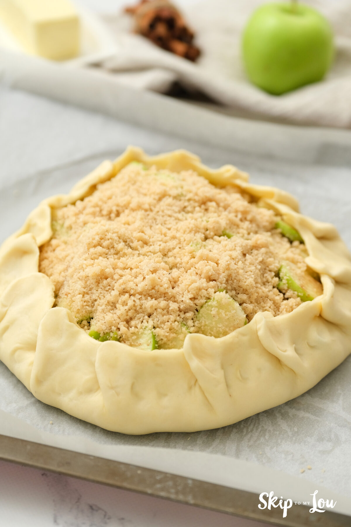 Apple crostate on a baking tray with the pastry edges crimped upwards and topped with the crumble mixture.