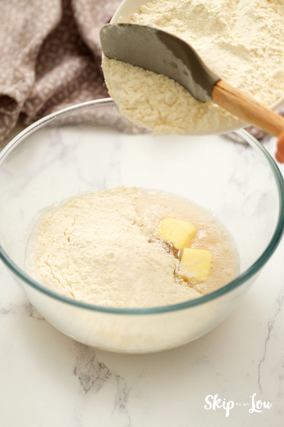 A bowl with wet ingredients with flour and butter being added.