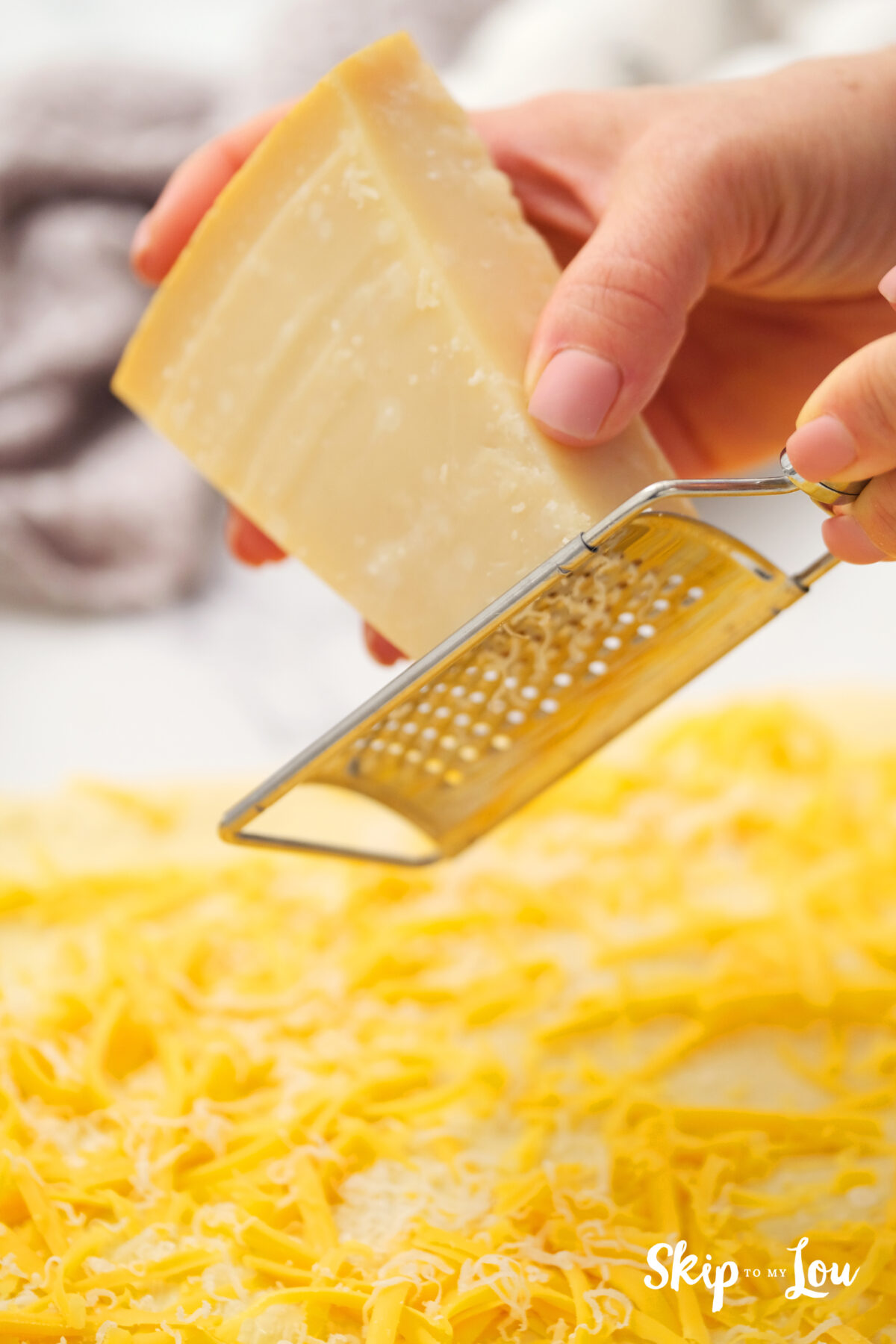 Parmesan being grated onto the dough which is already covered in cheddar cheese.