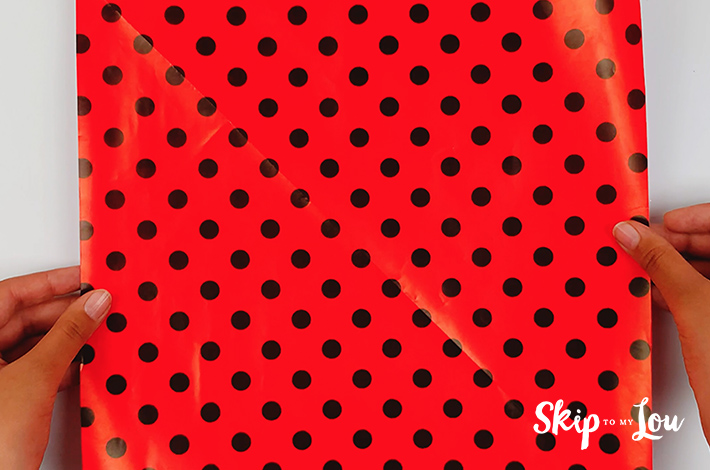 Two hands holding a square piece of wrapping paper with black dots on it.